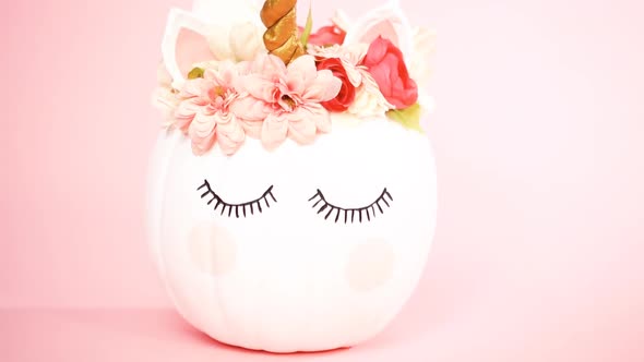 White unicorn pumpkin decorated with flowers on a pink background.