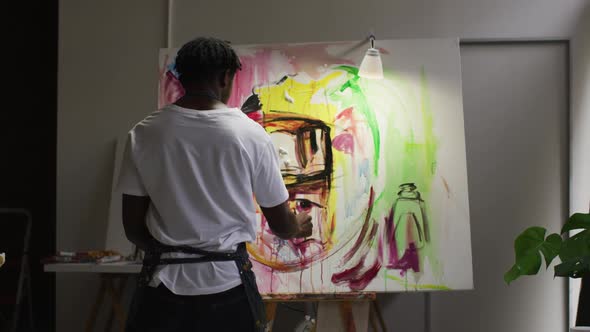 Rear view of african american male artist wearing apron painting on canvas at art studio