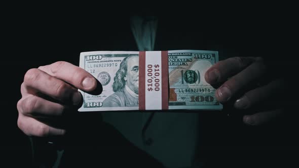 Businessman in Suit Shows Stack of 10000 American Dollars on Black Background