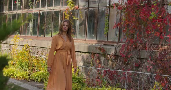 Mysterious Caucasian Woman Walking By Building Covered with Red Bushes and Smiling