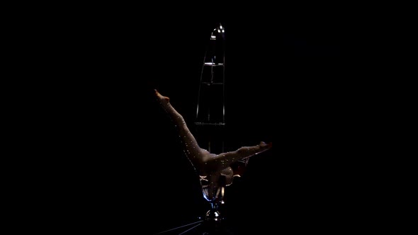 Girl Gymnast on One Arm Performs Gymnastic Stunts on a Rotating Structure Moon . Black Background