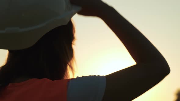 Woman Engineer Takes Off Her Protective Helmet on Before Work at Sunset or Sunrise