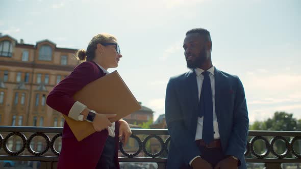 Young Multiethnic Business Couple Talking and Smiling Outdoor Leaning on Embankment Fence