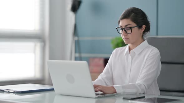 Indian Businesswoman Looking at Camera while using Laptop in Office