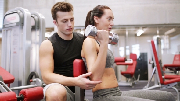 Young Couple With Dumbbell Flexing Muscles In Gym