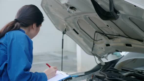 Asian female mechanic examining car, putting thumb up, and smiling.