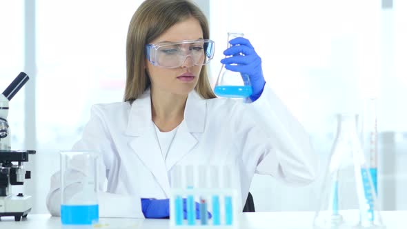 Female Scientist Looking at Blue Solution in Flask in Laboratory