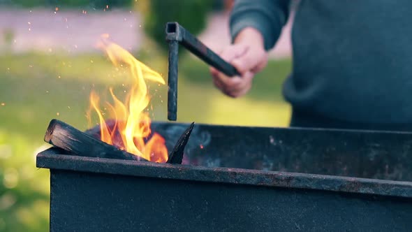 CU, Slow Motion: Man Pushes the Burning Firewood in the Brazier with Poker