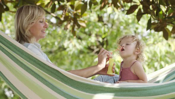 Happy mother play with her blue-eyed little baby girl, blowing soap bubbles together lying on the ha