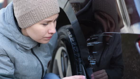 Young woman sadly examines fresh scratches on the bumper of her car