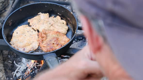 Man Cooking Fried Pork Chops in Oil in Frying Pan Over Fire Outdoor Fatty Meat