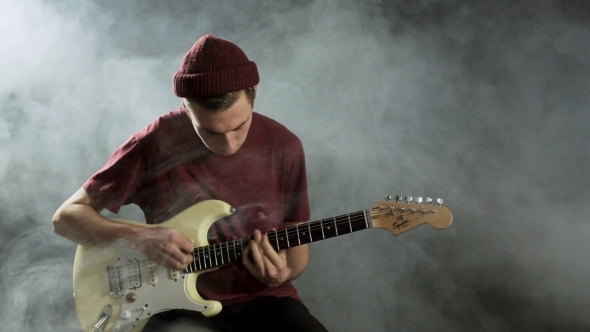 Young Guy Playing Guitar In a Dark Studio In Smoke