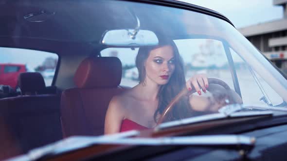 Bitchy Woman is Sitting in Parked Car and Looking Forward Lying Hand on Rudder