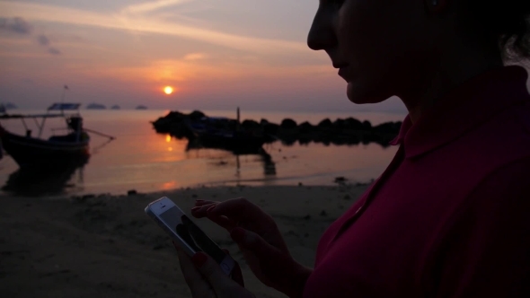 Female Using Smartphone On Beach Against Sunset