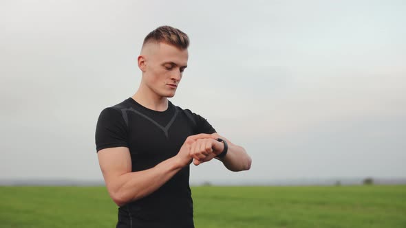 The Athlete is Standing on the Field and Choosing the Type of Training on His Watch