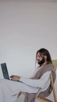 Jesus Sits in a Schizlong and Works at a Computer on a White Background