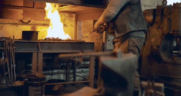 Blacksmith Turns the Coals in the Furnace