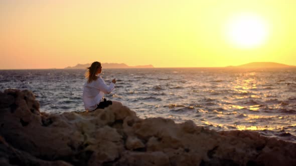 Slender Blonde in Black Short Shorts and White Shirt Fluttering in Wind Sit on Mountain Against