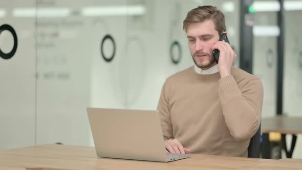 Creative Young Man Talking on Phone While Working on Laptop