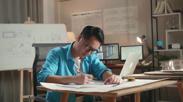 Asian Man Engineer With A Laptop Drawing Blueprint At The Office