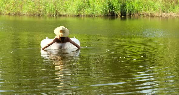 Woman in swimsuit and straw hat is floating with an inflatable circle in lake