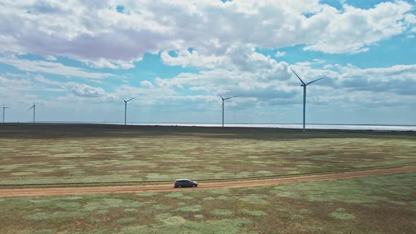 Car Moving By Rustic Road on Wind Electric Generators Background