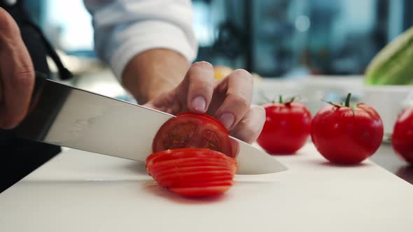 Professional restaurant kitchen, close-up: Chef cuts tomatoes with a knife