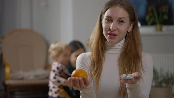 Portrait of Thoughtful Young Caucasian Mother Choosing Between Drugs and Fruits