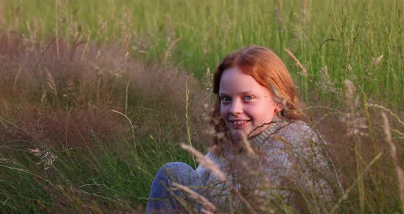 Cute Beautiful Teenager Girl with Long Red Hair Sitting on the Grass on Summer Field Enjoying the