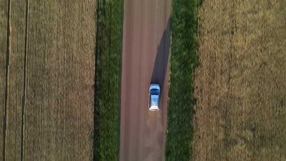 Aerial vertical shot of minivan driving along dirt road in rural Canada. Drone followingement of car