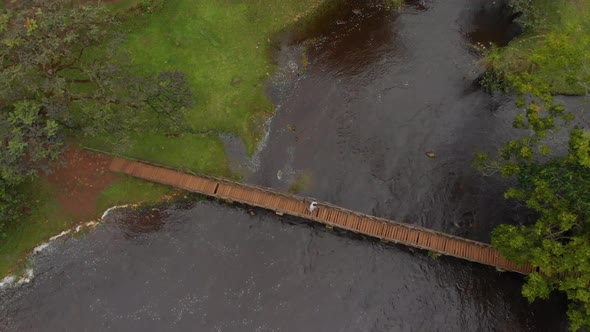 Aerial drone shot of African walking across a traditional foot bridge over a river in the jungle.