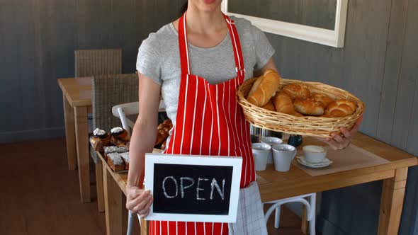 Portrait of female baker holding baguettes and open signboard