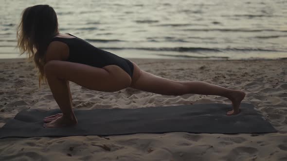 Sunset Beautiful and Calm Woman Practices Yoga on a Sandy Beach Using a Mat