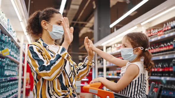 Happy Mom and Daughter Wearing Masks in the Supermarket Clap Each Other Hand in Hand