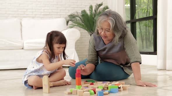 Elderly grandmother with Asian granddaughter Play wooden toys together in the living room