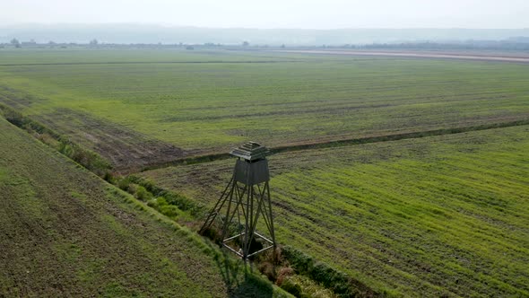 Rotating aerial view of an empty wooden hunting lookout in the middle of farming fields in rural Slo