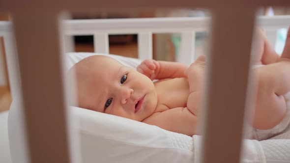 a Newborn Baby Lies in a White Crib in Cocoonababy for Newborns View Through the White Slats on the