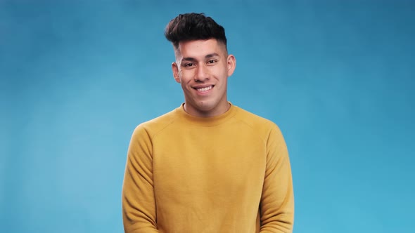 Young man smiling at the camera while standing over an blue background. Slow motion