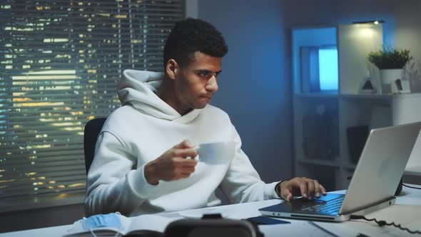 Handsome Multiracial Man Drinking a Cup of Coffee and Working on Computer at Night