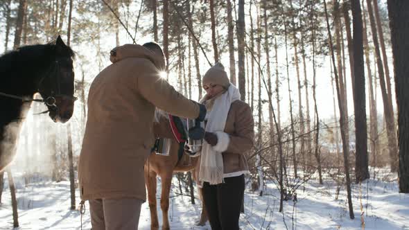 Couple Drinking Hot Tea during Horseback Riding in Winter Forest