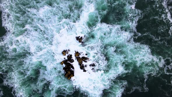 Aerial - Drone rises from rock in ocean, incessant pounding of waves