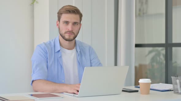 Creative Man Looking at Camera While Using Laptop in Office