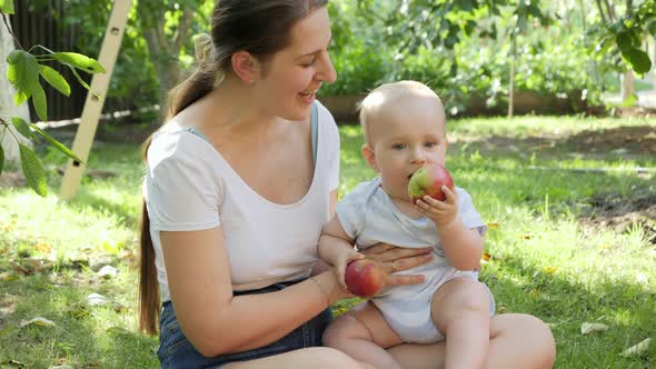 Portrait of Little Smiling Baby Boy Holding and Biting Ripe Apple at Orchard