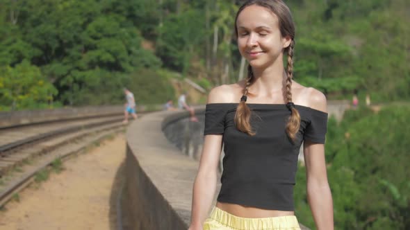 Girl Sits on Bridge Barrier and Smiles at Tropical Nature