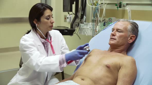 Nurse Examining Mature Male Patient In Hospital Bed