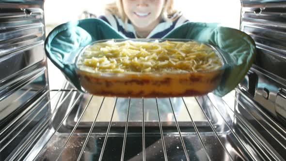 Woman Putting Dish Of Lasagne Into Oven To Cook