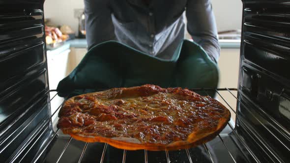 Man Taking Cooked Pepperoni Pizza Out Of The Oven alt