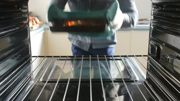 Man Taking Tray Of Roasted Vegetables Out Of The Oven