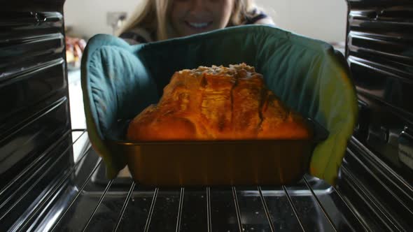 Woman Taking Baked Loaf Of Bread Out Of The Oven alt