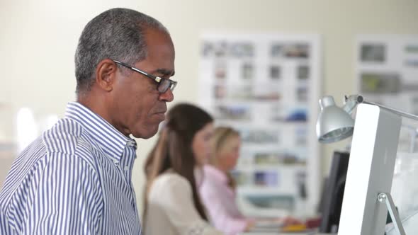 Man Using Computer At Desk In Busy Creative Office